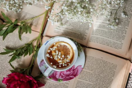 Cup of tea with lemon and flowers on old book background.