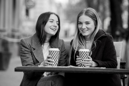 Two young women sitting at a table in a cafe, drinking coffee and laughing