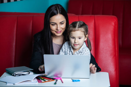 Mother and daughter using a laptop while sitting at the table in a cafe