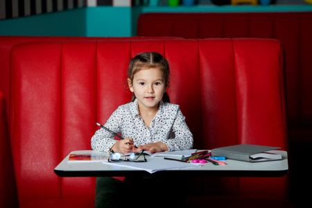 Portrait of a cute little girl sitting at the table and drawingの写真素材