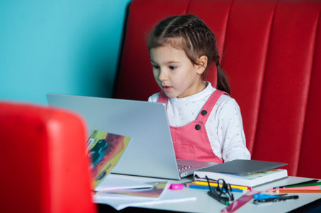 Cute little girl sitting at the table and working on a laptop