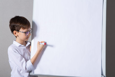 boy in glasses draws on a white sheet of paper with a marker