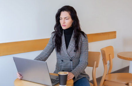 Serious businesswoman using laptop while sitting at table in coffee shop