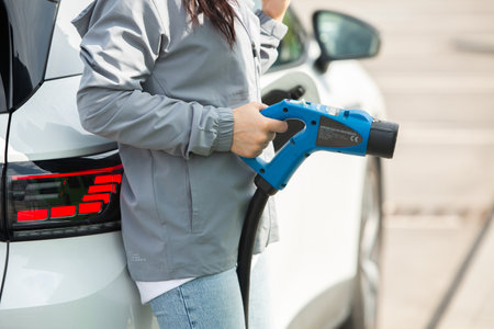 Close up of a young woman charging her electric car at gas stationの写真素材