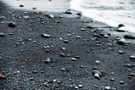 Black sand beach with small pebble stones and foamy wavesの写真素材