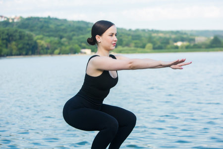 Young woman practicing yoga on the beach by the lake. Healthy lifestyle.