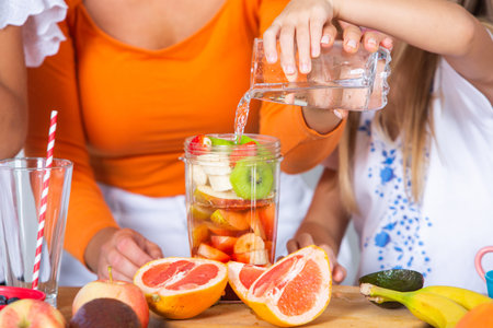 Close up of female hands pouring water from bottle into glass with fruitsの写真素材