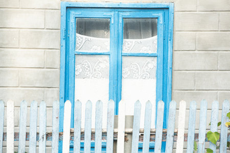 Old blue wooden window with white wall and blue picket fence.の写真素材