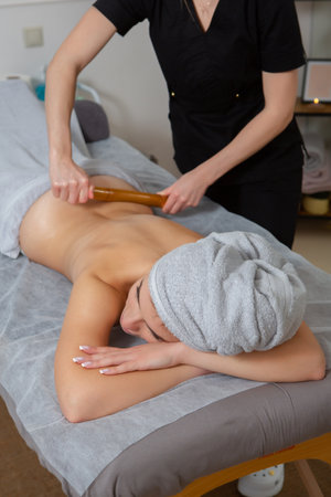 Beautiful young woman enjoying massage in spa salon. Relaxed brunette girl lying on massage bed with closed eyes during spa treatment procedure.の写真素材