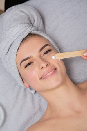 Beautiful woman in spa salon applying cosmetic cream on her face.
