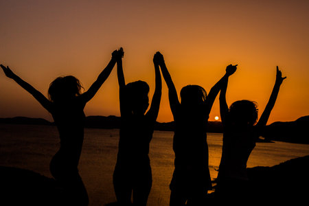 Silhouette of a group of young people dancing on the beach at sunsetの写真素材