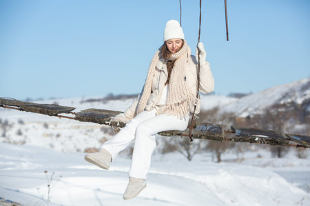 Young woman sitting on a swing in a snowy park. Winter season.