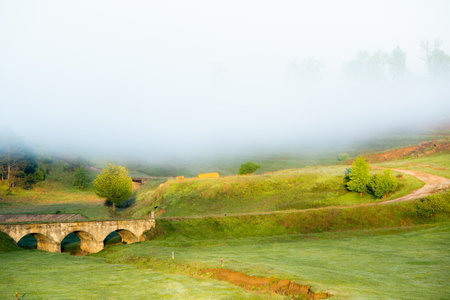 Old stone bridge in the foggy meadow. Tuscany, Italyの写真素材