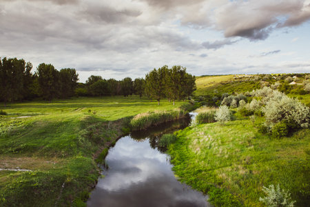 Beautiful summer landscape with river and green meadow under cloudy sky