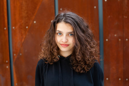 Portrait of a beautiful young woman with long brown curly hair on the street