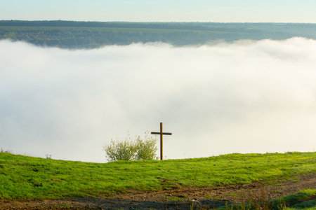 Cross on the hillside in the fog. View from the hill.の写真素材