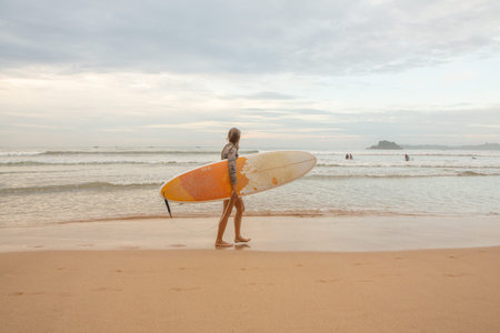 Surfer girl with surfboard on the beach at sunset or sunrise