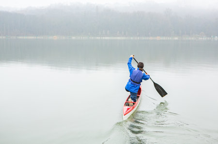 Man paddling a boat on a lake in the foggy morning.Photo of the capital of the Republic of Moldova, Chisinau during the winter fog.の写真素材