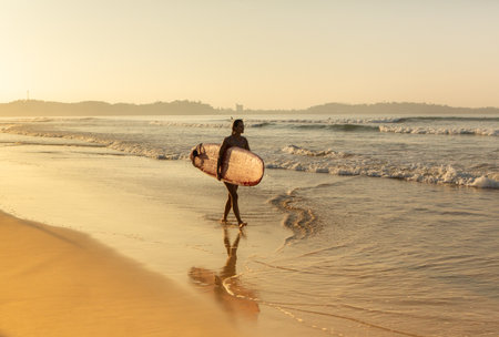 Silhouette of a woman carrying a surfboard on the beachの写真素材