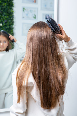 Young woman combing her long brown hair in front of mirror at homeの写真素材