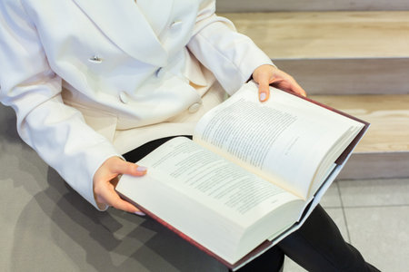 Woman reading a book in a library, closeup of hands.