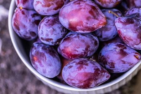 Ripe plums in a white bowl on a background of nature.