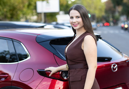 Young beautiful woman standing near a red car on the street. Front view.