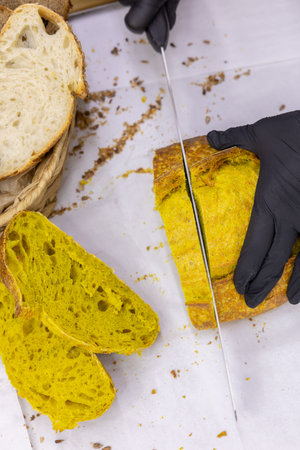 Cutting bread with a knife on a white tablecloth, top view