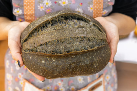 Hands holding a freshly baked loaf of rye bread in a bakeryの写真素材