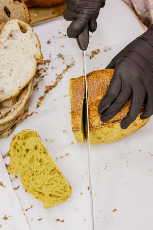 Female hands in black gloves cut a loaf of bread on a cutting board.