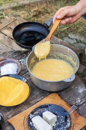 Man Preparing Rustic Polenta with Sheep Cheese on Open Fire. Authentic Countryside Cooking. Rustic...