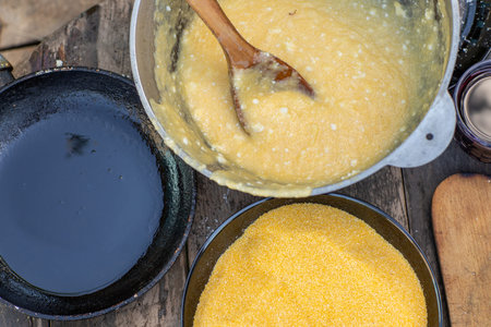 Man Preparing Rustic Polenta with Sheep Cheese on Open Fire. Authentic Countryside Cooking. Rustic...