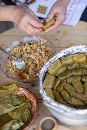 Woman preparing stuffed grape leaves with meat and rice in the kitchen.