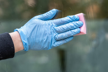 hand in blue glove cleaning window with sponge and detergent, closeupの写真素材