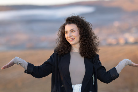 Young beautiful girl with curly hair in a black jacket on the background of nature.