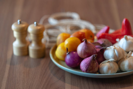 Onion, garlic, tomato, pepper and salt shaker on wooden tableの写真素材