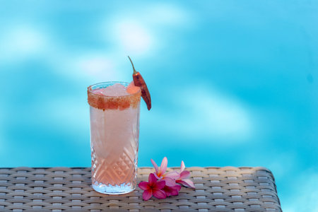 Alcoholic cocktail with pink plumeria on the swimming pool background