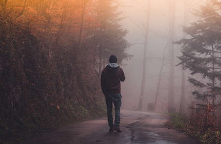 Man walking alone on a road through a foggy forestの写真素材