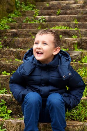 smiling little boy sitting on the stairs outdoorsの写真素材