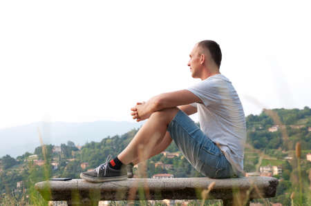 young man sitting on a bench and admire the city viewsの写真素材