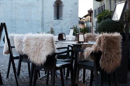 tables and chairs with fur covers in a cafe in Piazza Duomo and the city of Trento, Italyの写真素材