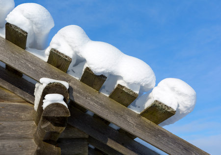 Snow drift on roof after of snowfalls on sunny day. Old Wooden house in the snow.