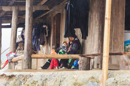 Sa pa, Vietnam-December 13, 2013. Vietnamese Black Hmong women with a children are siting in front their home rainy day in the village house at Muong Hoa Valley on December 13, 2013 in Sa Pa, Vietnamのeditorial素材