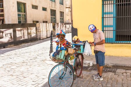 Havana, Cuba-October 07, 2016. Man at historical part of Old Havana with two dachshund breed dogs on the bicycle, dressed in colorful outfit of cuban flag to attract tourist.のeditorial素材