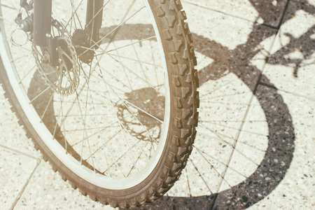 Bycycle front wheel shadow silhouette and tire view on urban concrete tile surface backgroundの写真素材