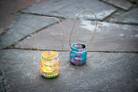Two colorful glass jars with wire handle candle lamps on stone outdoor tile, kids activities and handmade idea conceptの写真素材