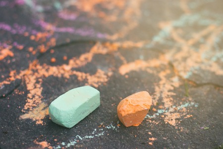 Two small green and orange piaces of chalk on a sidewalk surface close up view