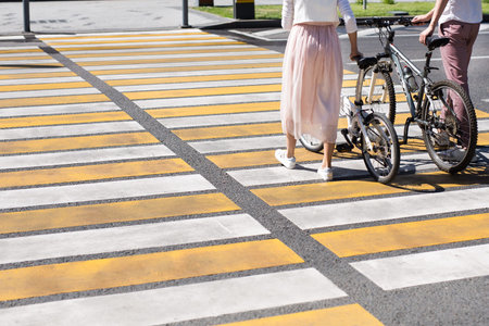 young woman legs and man legs walking with bike across of cross road