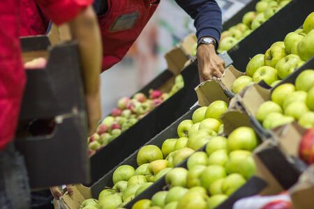 Young man seller lays out fresh fruits of the box on the grocery storeの写真素材