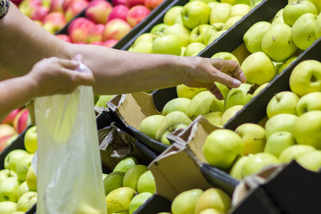 Old woman selecting fresh apples in grocery store produce department and putting it in plastic bag.の写真素材